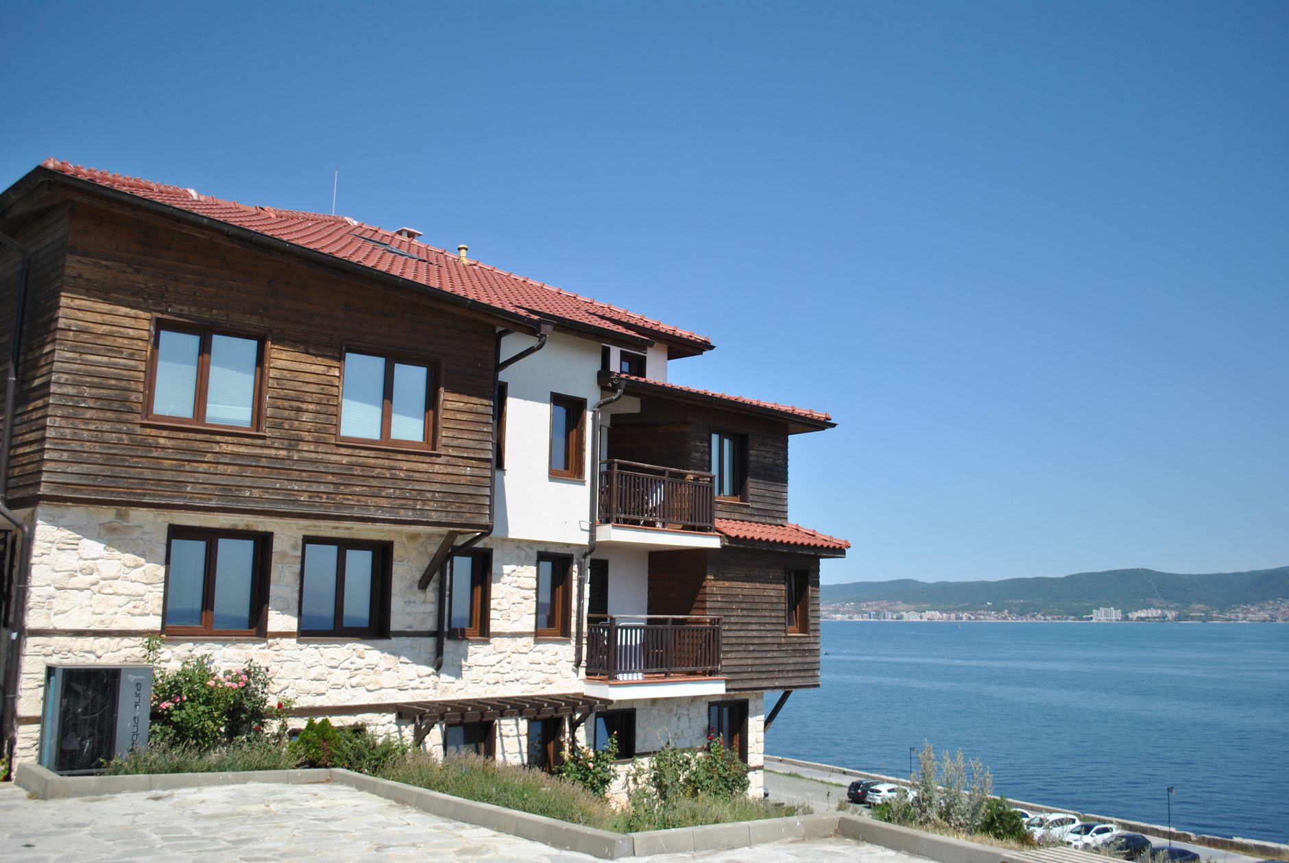Traditional wooden house by the sea, offering a scenic coastal view under a clear blue sky.